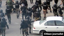 A riot police officer breaks window on a car during protests by opposition critics in Tehran.