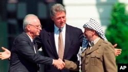Premierul israelian Yitzhak Rabin (st.) și liderul palestinian Yasser Arafat își dau mâna la semnarea acordului de pace („de la Oslo”) dintre Israel și palestinieni, sub privirile președintelui american Bill Clinton. Washington, 13 septembrie 1993 (AP)