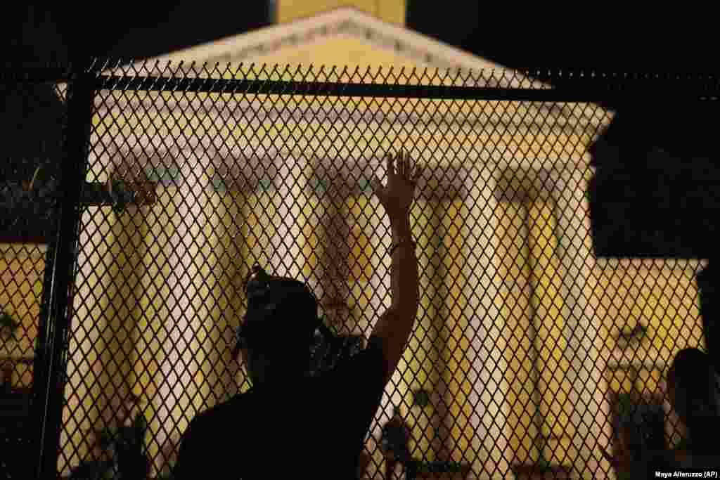 A protester calls out to police standing guard behind security fencing at St. John's Episcopal Church, near the White House, early Wednesday, June 24, 2020, amid continuing anti-racism demonstrations following the death of George Floyd, a Black man who was restrained by police in Minneapolis. (AP Photo/Maya Alleruzzo)
