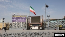 Un steag negru și un steag iranian flutură în vânt, în Teheran, într-o piață aproape goală, pe 5 martie 2026.