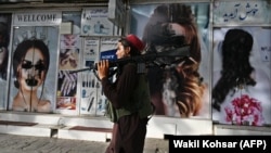 A Taliban fighter walks past a beauty salon in Kabul where images of women have been defaced.