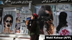 A Taliban fighter walks past a beauty salon with images of women defaced using spray paint in the Shar-e Naw neighborhood in Kabul.