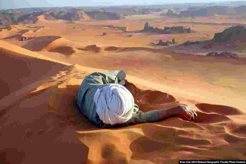 "A well earned rest in the Sahara" by Evan Cole. Summit of Tin-Merzouga, Tadrat, Tassili N'Ajjer National Park, Algeria. "This photo, of Moussa Macher, our Touareg guide, was taken at the summit of Tin-Merzouga, the largest dune (or erg) in the Tadrat region of the Sahara desert in southern Algeria. Moussa rested while waiting for us to finish our 45 minute struggle to the top. It only took 10 minutes of rolling, running and jumping to get to get back down. The Tadrat is part of the Tassili N'Ajjer National Park World Heritage Area, famous for its red sand, and engravings and rock paintings of cattle, elephants, giraffes and rhinos that lived there when the climate was milder."