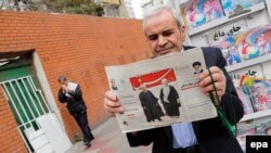 An Iranian man holds a copy of the daily Sharq newspaper with pictures of Iranian President Hassan Rohani and headline reading 'Decisive victory for the reformist' outside a kiosk in Tehran. Undated