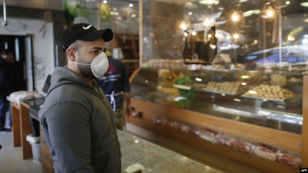 یک فلسطینی ساکن نوار غزه با ماسک بر صورت در صف انتظار شیرینی‌فروشی.