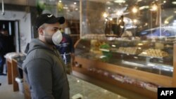 یک فلسطینی ساکن نوار غزه با ماسک بر صورت در صف انتظار شیرینی‌فروشی.