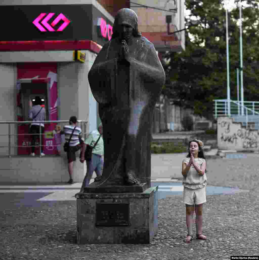A girl imitates the Mother Teresa monument in central Skopje. Born to ethnic Albanians under Ottoman rule, Anjezë Gonxhe Bojaxhiu dedicated her life to the poor and sick of Calcutta and was beatified in 2016.