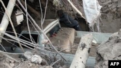 A man inspects a destroyed car trapped under the rubble of a house in the eastern village of Shaj.