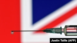 Egy fecskendő cseppjében az Egyesült Királyság zászlaja tükröződik. Az AstraZeneca és Boris Johnson brit miniszterelnök 2021. január 28-án védelmébe vette a gyógyszergyártó cég vakcináját, miután a németek közölték, hogy azt nem szabad 65 évesnél idősebbeknek adni.