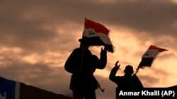 IRAQ -- Fighters with Iran-backed militias in Iraq known as the Popular Mobilization Forces, wave Iraqi flags while mourners and family members prepare to bury the body of Abu Mahdi al-Muhandis, deputy commander of Iran-backed militias who was killed in a