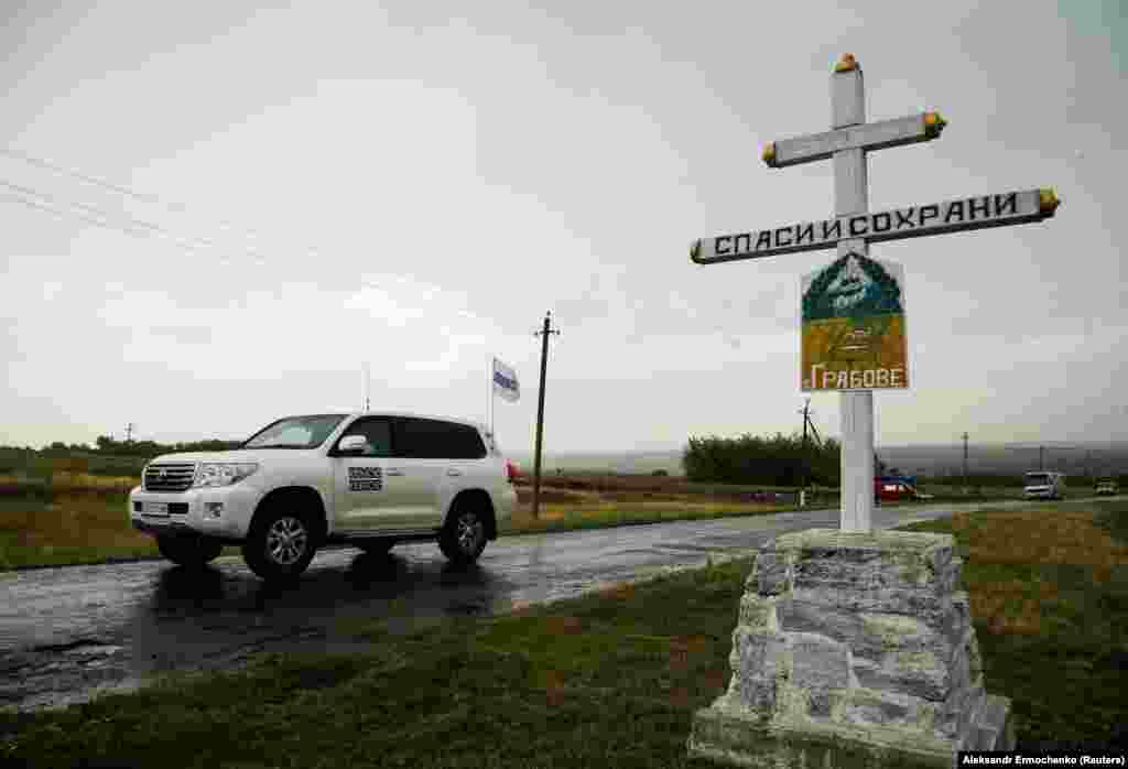 Monitors from the Organization for Security and Cooperation in Europe drive past a cross near the crash site of Malaysia Airlines Flight 17, which was shot down six years before over rebel-held territory on July 17, 2014, outside the village of Hrabove in Ukraine&#39;s Donetsk region. (Reuters/Aleksandr Yermochenko)