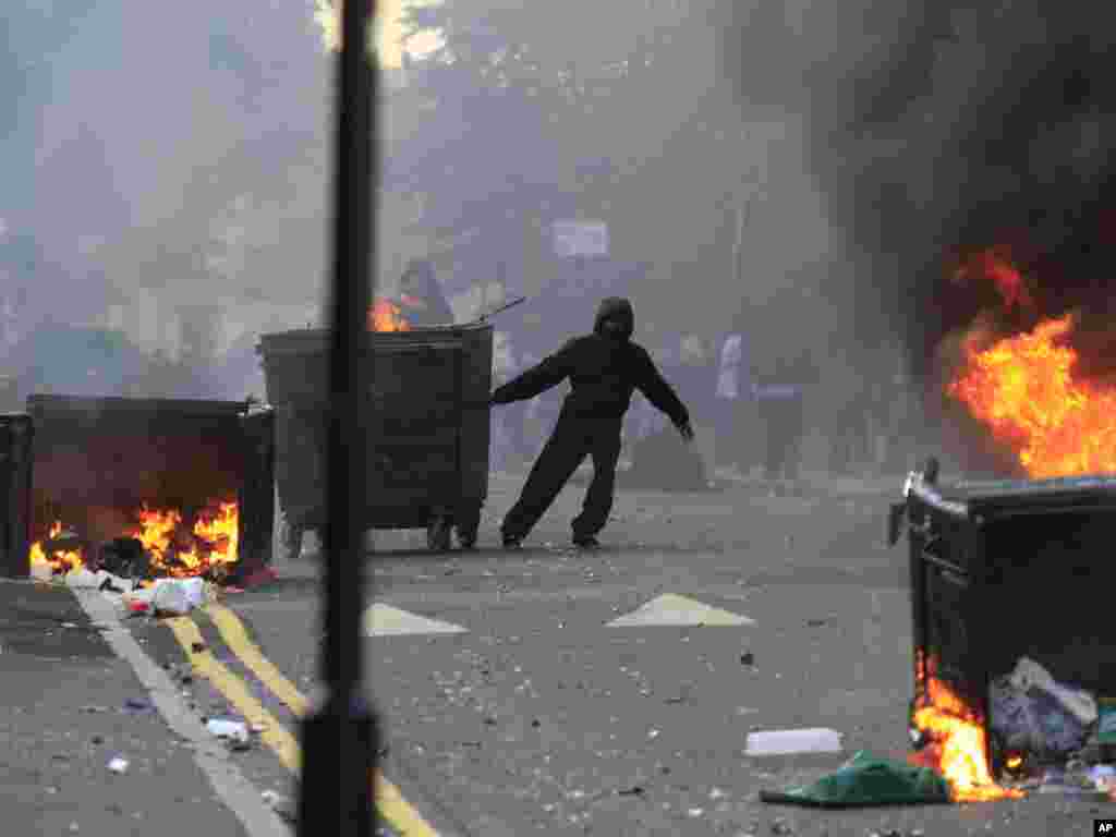 A masked youth pulls a burning garbage bin set on fire by rioters in Hackney, east London, on August 8. Photo by Lefteris Pitarakis for AP