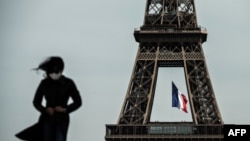 Женщина в маске идет, когда французский национальный флаг развевается над Эйфелевой башней на заднем плане в Париже в первый день ослабления во Франции мер по блокировке, пандемии COVID-19, вызванной новым коронавирусом. 11 мая 2020 г., 