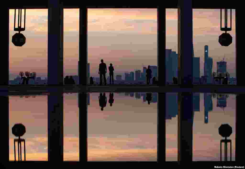 People are reflected in a puddle as they watch the sunset in Moscow.&nbsp;