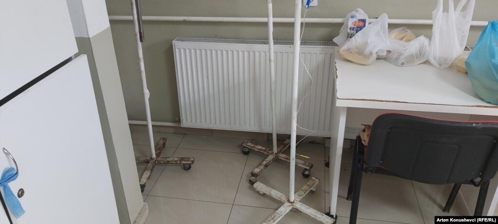 Qese të mbushura me pemë, lëngje e ushqime në një tavolinë në dhomën e pacientëve. Aty vërehen edhe mbajtëse të infuzioneve të vjetra e të ndryshkura.