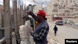 Sectorul israelian al construcțiilor este suprasolicitat și din cauza practicii extinderii așezărilor evreiești din teritoriile palestiniene. În imagine: un muncitor palestinian lucrează pe un șantier într-o așezare evreiască de lângă Ierusalim, martie 2013.