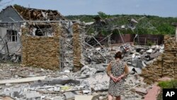 Egy asszony sétál az éjszakai bombázásban lerombolt háznál az ukrajnai Szlovjanszkban 2022. június 1-jén