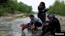 A group of people who tried to cross the Greek-Macedonian border takes a rest after crossing a small river on their way back to a makeshift camp for refugees and migrants at the border near the village of Idomeni, Greece, May 12, 2016. 