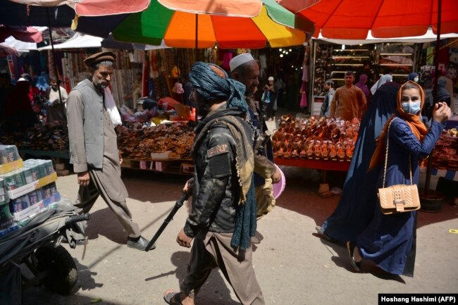 Talibanski borac prolazi pored kupaca na pijaci Mandaci u Kabulu, 1. septembar 2021.