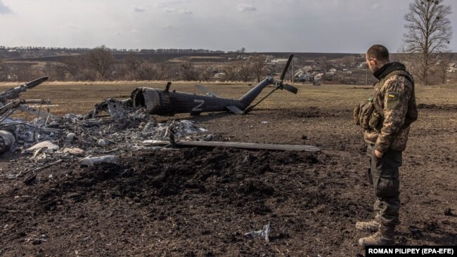 Украинский военнослужащий возле уничтоженного российского вертолета с буквой «Z», символом российского вторжения в Украину, в отбитой украинской армией деревне Малая Рогань возле Харькова, 31 марта 2022 года