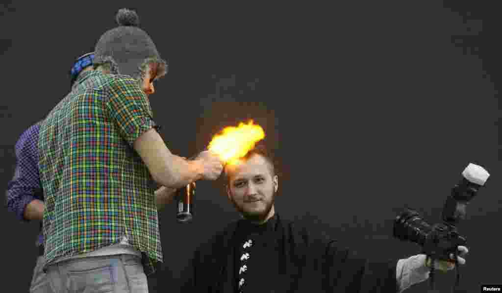 A volunteer takes a picture of himself receiving a haircut as a hairstylist uses fire to &quot;cut&quot; the hair during a &quot;Barber Trash&quot; show on the first day of the annual Ideal of Beauty spring festival in the Siberian city of Krasnoyarsk, Russia (Reuters/Ilya Naymushin)