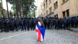 A demonstrator draped in the Georgian national and EU flags stands in front of police blocking the way to the parliament building in Tbilisi during an opposition protest against a controversial "foreign agent" law in May. 