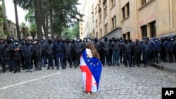 Грузия менен Евробиримдиктин желектерин жамынган демонстрант кыз полиция кызматкерлеринин алдында турат. 14-май, 2024-жыл. Тбилиси.
