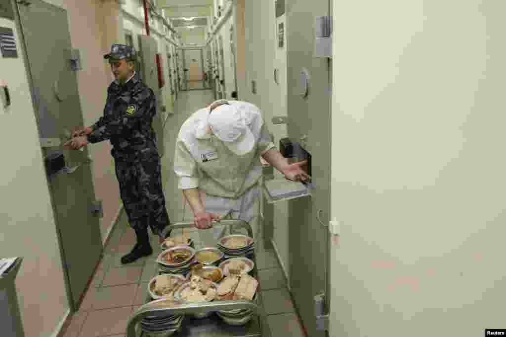 A security officer stands next to an inmate serving dinner to other prisoners inside a maximum-security zone.