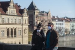 Чоловік та жінка у захисних масках стоять на Карловому мосту, Прага