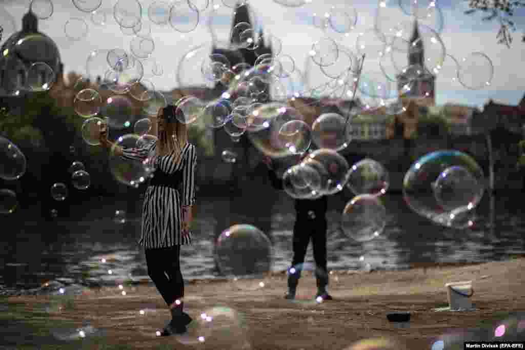A woman takes a selfie as a man blows bubbles on the bank of the Vltava River in Prague. (epa-EFE/Martin Divisek)