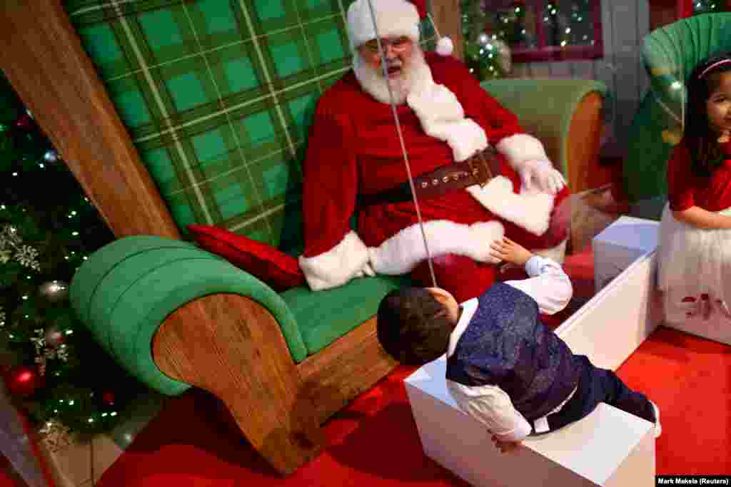 Хлопчик тягнеться до Санта-Клауса, який сидить за перегородкою з плексигласу в торговому центрі Willow Grove Park. Віллоу-Гроув, штат Пенсильванія, США