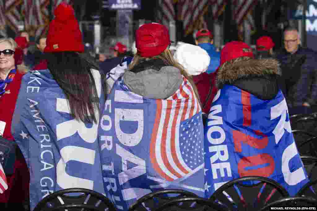 Emberek zászlókkal a hátukon vesznek részt a Donald Trumpot támogató rendezvényen.