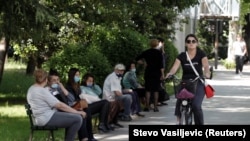 Женщина едет на велосипеде мимо людей, которые ждут автобус в Подгорице. Черногория, 25 мая 2020 года