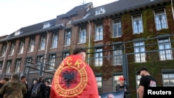 Një protestues i mbështjellë me flamur të Ushtrisë Çlirimtare të Kosovës, qëndron pranë selisë së Dhomave të Specializuara të Kosovës në Hagë, teksa gjykatësi shqipton aktgjykimin ndaj ish-krerëve të UÇK-së, në Hagë, Holandë, 16 shtator 2026.