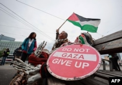 Un activist, fluturând un steag palestinian alături de un banner cu mesajul „Nu abandonați Gaza”, în timpul unui protest la Viena, cu sloganul „Fără muzică pentru execuții. Fără poleială peste vărsare de sânge”