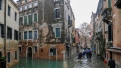 Njerëzit ecin në rrugët e përmbytura nga uji në Venecia.