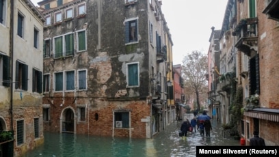 Njerëzit ecin në rrugët e përmbytura nga uji në Venecia.