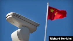 Китайски флаг се вее близо до охранителна камера Hikvision, която наблюдава кръстовище в Пекин, вторник, 8 октомври 2019 г.