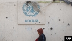 Një grua palestineze kalon pranë logos së agjencisë së OKB-së për ndihmën e palestinezëve, UNRWA. Rafah, 28 maj 2024. 