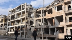 Syrians walk past destroyed buildings in the former rebel-held Ansari district in the northern Syrian city of Aleppo on December 23, after Syrian government forces retook control of the whole city.