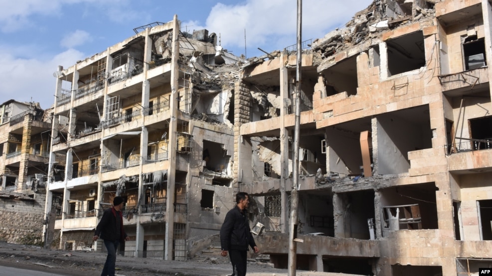 Syrians walk past destroyed buildings in the former rebel-held Ansari district in the northern Syrian city of Aleppo on December 23, after Syrian government forces retook control of the whole city.