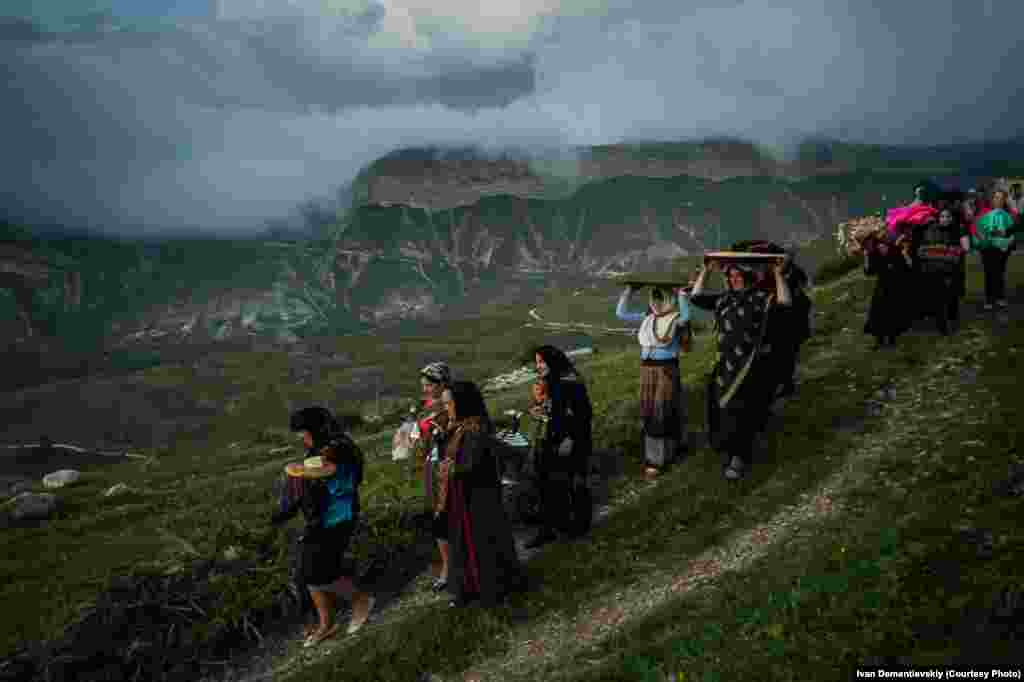 Village women transport a dowry for the bride which consists of useful items such as carpets, jugs, and blankets while also comprising ornaments and money.