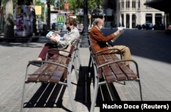Dy të moshuar – që kanë veshur maska – lexojnë gazetën në Barcelonë të Spanjës.