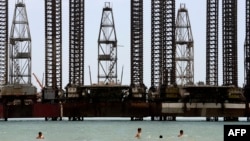 Azeris cool off in the Caspian Sea with offshore oil rigs in the background in Baku.