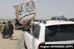 People wave a Taliban flag as they drive through the Pakistani border town of Chaman on July 14, 2021, after the Taliban claimed it had captured the town of Spin Boldak across the border in Afghanistan.
