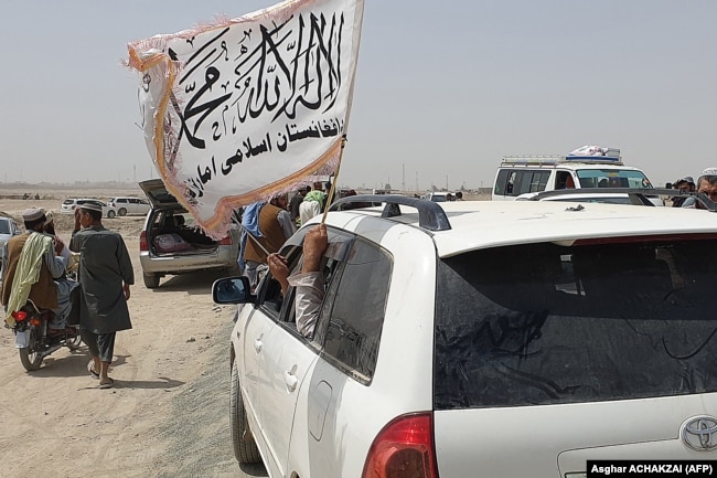 Njerëzit duke valëvitur flamurin e talibanëve teksa kalojnë kufirin me Pakistanin më 14 korrik 2021, pasi talibanët morën kontrollin e qytetit Spin Boldak, që gjendet në pjesën e kufirit të Afganistanit.