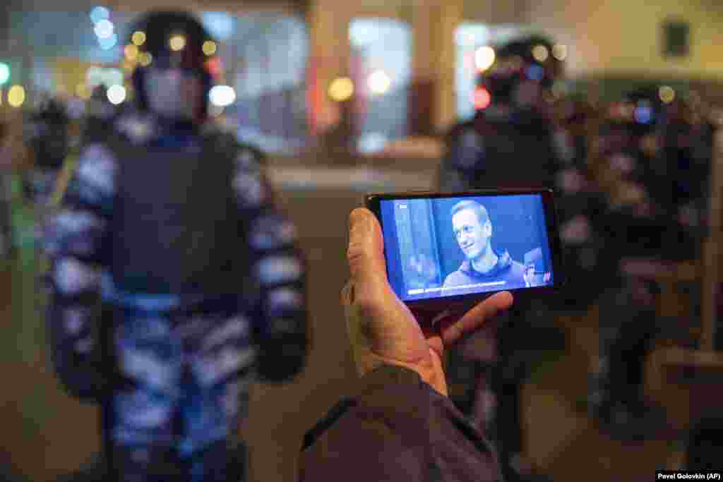 A journalist watches a livestream of the Navalny sentencing hearing as National Guard soldiers stand in front of the court in Moscow. The court converted a years-old suspended sentence to a prison term for a financial-crime conviction widely seen as politically motivated.