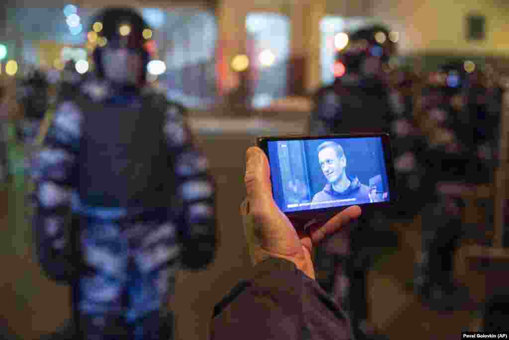 Një gazetar shikon në telefonin e tij, transmetimin direkt nga gjykata, ku Navalnyt iu shqiptua dënim me burg, teksa ushtarët e Gardës Kombëtare ruajnë gjykatën në Moskë. Kjo gjykatë ia shndërroi Navalnyt një dënim me kusht, në burg efektiv, për një rast lidhur me keqpërdorim fondesh. Ky rast ndaj Navalnyt, gjerësisht shihet si rast i motivuar politikisht.