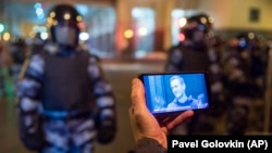 Egy újságíró Alekszej Navalnij orosz ellenzéki vezető bírósági tárgyalásának élő közvetítését nézi, miközben az orosz nemzeti gárda katonái őrködnek a moszkvai bíróság épülete előtt 2021. február 2-án.