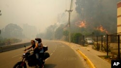 Banorët duke u evakuuar me motoçikletë nga zjarri në Vila del Mar, Kili, 3 shkurt 2024.